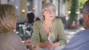 Woman sitting comfortably at a casual dinner gathering holding sparkling water while socializing naturally without alcohol.