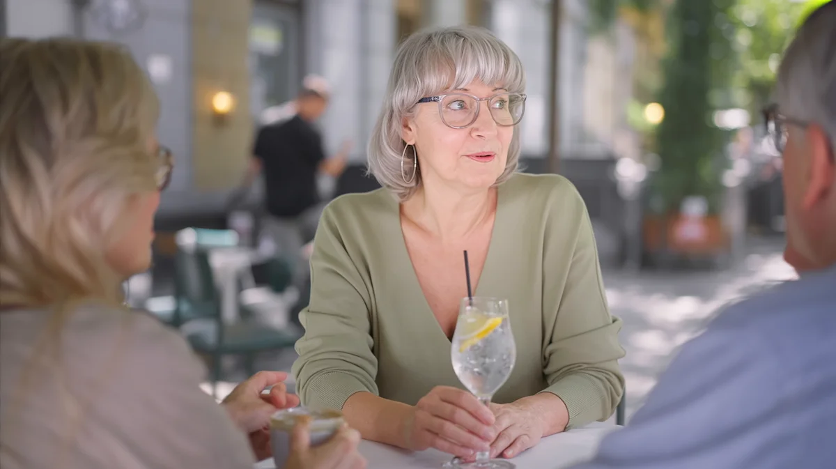 Woman sitting comfortably at a casual dinner gathering holding sparkling water while socializing naturally without alcohol.