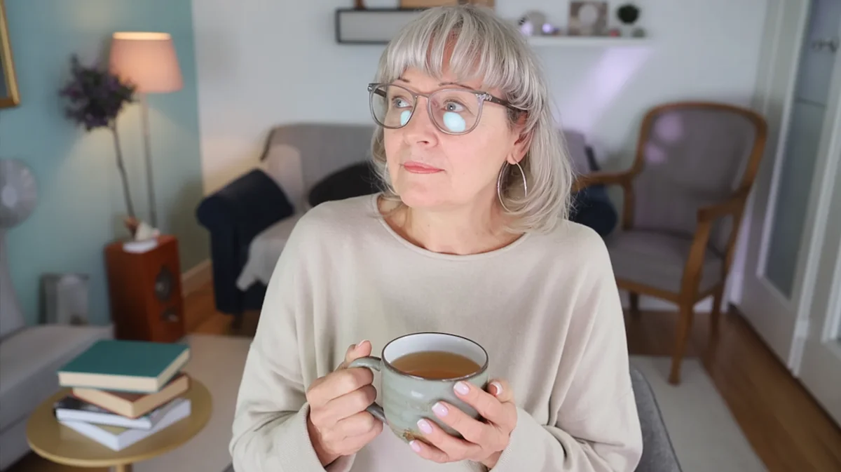 Woman sitting quietly in a softly lit living room at night holding a mug of tea while reflecting on life without alcohol.