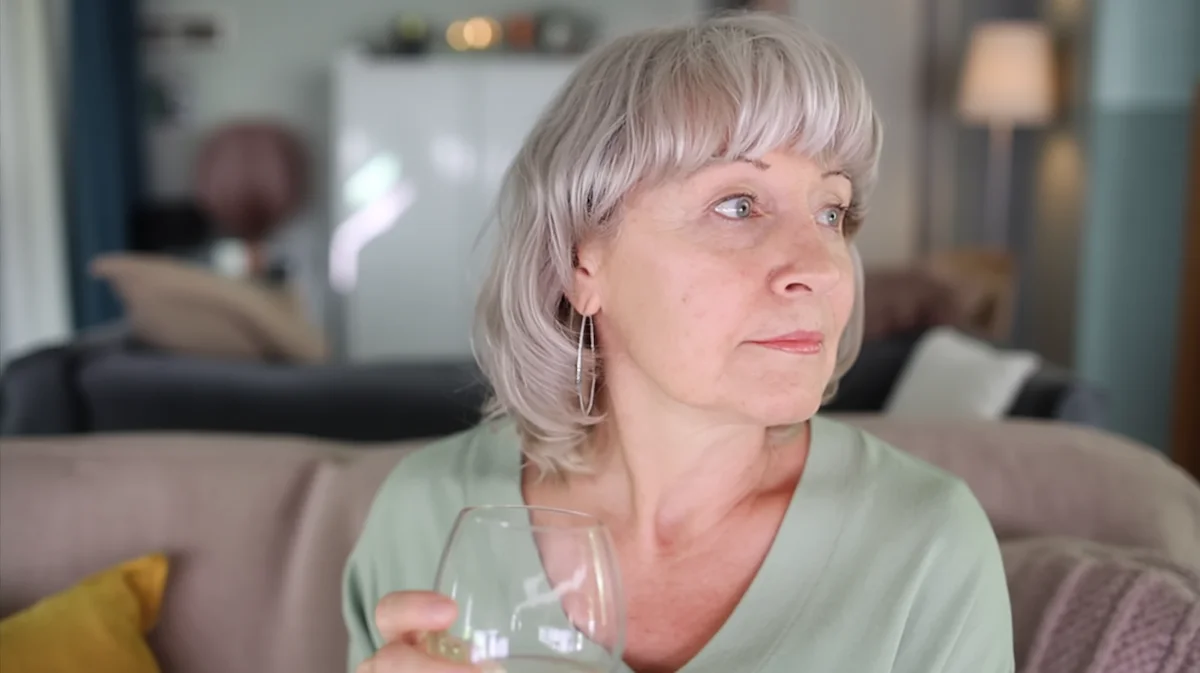 Woman sitting on couch holding wine glass looking away thoughtfully at home