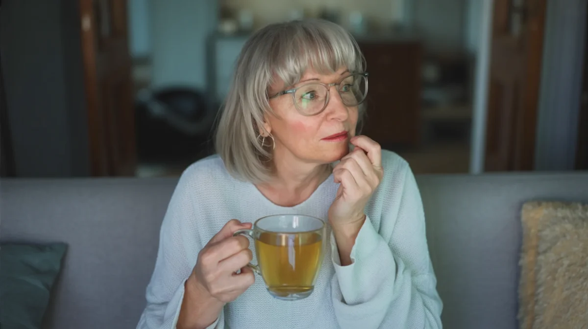 Caught Between Wanting Change and Wanting Comfort Woman sitting quietly at home in the evening, reflecting while hesitating during a familiar nightly drinking routine