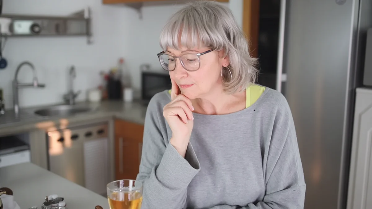 Woman in kitchen pausing and looking thoughtfully at a drink, reflecting a repeated drinking habit