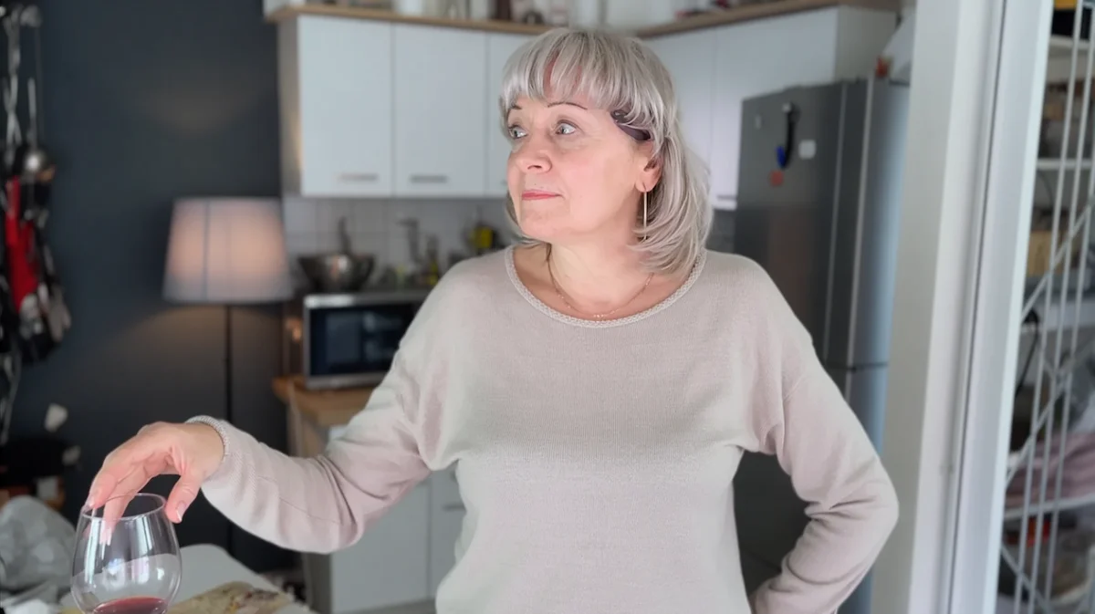Woman in kitchen at night hesitating with wine glass looking uncertain
