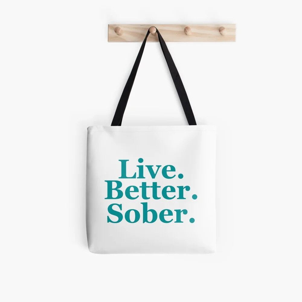 White tote bag with turquoise “Live. Better. Sober.” typography design.