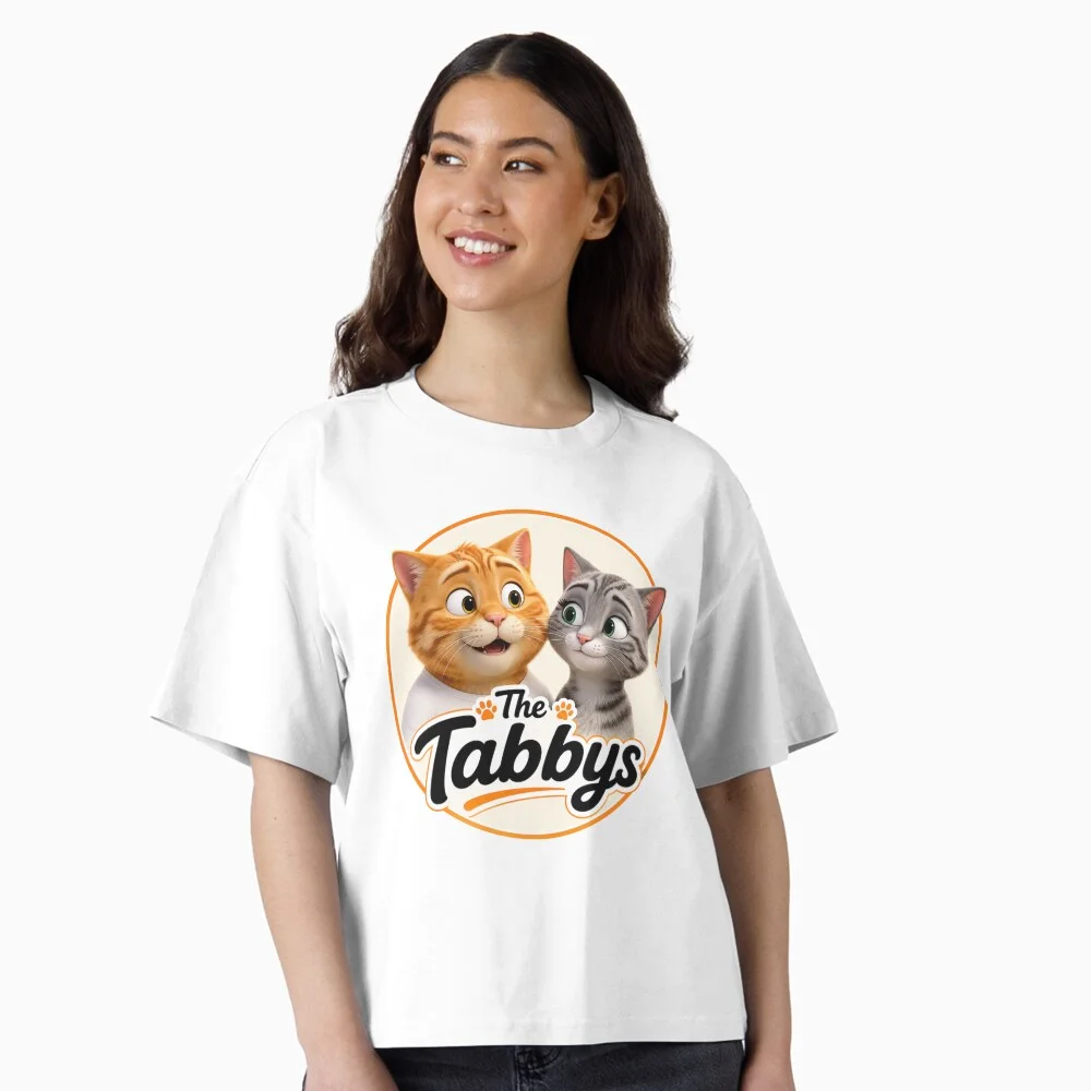 Woman wearing a white boxy T-shirt featuring The Tabbys logo with George and Maggie the tabby cats.